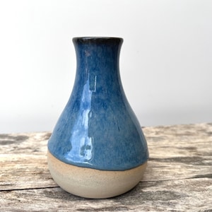Könnte beinhalten: Eine Keramikvase mit bauchiger Basis und engem Hals. Der obere Teil ist mit einer glänzenden, gesprenkelten blauen Glasur versehen, während der untere Teil ein unglasiertes, mattes beiges Finish aufweist. Der Übergang ist deutlich erkennbar.