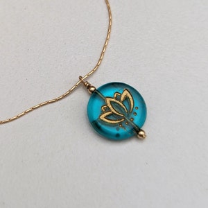 May include: A gold chain necklace with a turquoise blue pendant featuring a gold lotus flower design.
