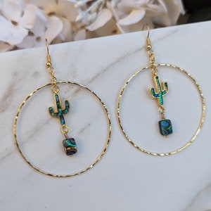May include: Gold hoop earrings with a green and blue abalone shell cactus charm dangling from each hoop.