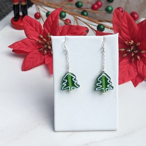 May include: A pair of silver dangle earrings with green and white glass Christmas tree charms.