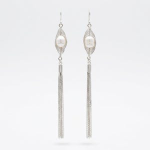 May include: A pair of silver-toned dangle earrings featuring a central white pearl encased in a delicate wire-wrapped cage design. Each earring hangs from a hook and terminates in a long, slender metallic chain tassel that adds movement.