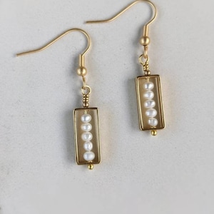 May include: Gold earrings with a rectangular frame and a row of white pearls hanging inside.