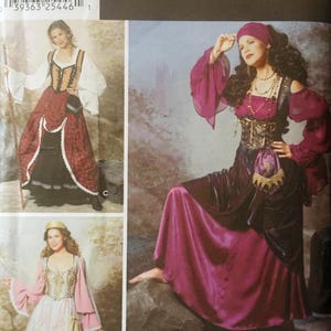 Op de afbeelding: Een Simplicity Costumes naaipatroon envelop 9966 voor de maten 14, 16, 18 en 20. De verpakking toont drie variaties van een historisch ogende jurk met lijfjes, lange mouwen en rokken, waarvan één versie inclusief een hoofddoek.