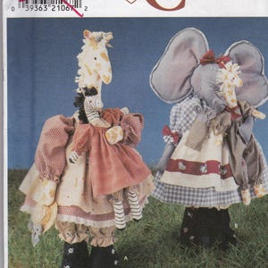 May include: Simplicity Crafts pattern featuring two stuffed animal dolls. One doll is a giraffe with a zebra, and the other is an elephant with a giraffe. Both dolls are wearing dresses and have black boots. The pattern is from Daisy Kingdom.