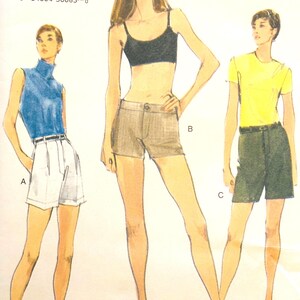 May include: A vintage Vogue sewing pattern with illustrations of three outfits: a blue turtleneck top with white shorts, a black crop top with tan shorts, and a yellow t-shirt with dark green shorts. The pattern size is 8-10-12.
