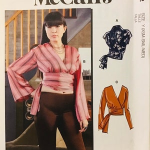 May include: A sewing pattern for a wrap top with three different views. The pattern includes instructions for making the top in three different colors: pink and white stripes, black and white floral print, and brown. The pattern is for sizes X-Small, Small, and Medium.