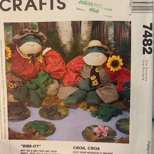 Puede incluir: Patrón de McCall's Crafts para muñecos de rana. La imagen muestra dos muñecos de rana, cada uno con sombrero y atuendo estampado. Los muñecos miden aproximadamente 60 cm de alto. El patrón incluye instrucciones para hacer los muñecos de rana y sus bebés.