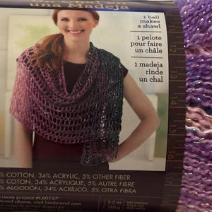 May include: A ball of purple yarn with a shimmering effect. The label shows a woman wearing a shawl made from the yarn. The label also states that one ball makes a shawl. The yarn is 61% cotton, 34% acrylic, and 5% other fibre.