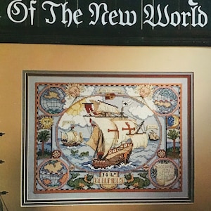 May include: A framed cross-stitch design depicting a ship sailing on the ocean with the text "Discovery of the New World" and "1492 Columbus".
