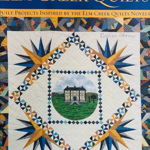 Puede incluir: Portada del libro "ELM CREEK QUILTS" con fondo azul oscuro y letras doradas. El diseño del edredón presenta una ilustración de una casa en el centro, enmarcada por motivos de estrellas en azul, dorado y blanco, con un borde de retazos.