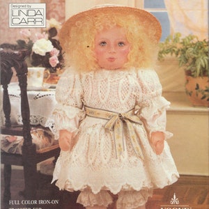 Puede incluir: Una muñeca blanca con un vestido de encaje blanco con una cinta amarilla, un sombrero blanco y zapatos blancos. La muñeca está sentada en un suelo de madera. La muñeca forma parte de la colección de muñecas Vogue.