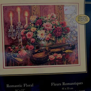 Könnte beinhalten: Gerahmtes Kreuzstich-Set mit dem Titel "Romantic Floral" mit einem detaillierten Blumenarrangement in einer Vase, mit brennenden Kerzen und einer Geige. Das Design misst 41 x 33 cm und enthält einen farbcodierten Fadensortierer.