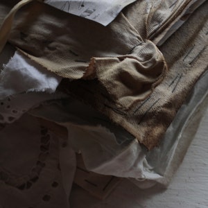 Puede incluir: Una pila de trozos de tela viejos, desgastados y deste&ntilde;idos en tonos de blanco, crema y marr&oacute;n. La tela est&aacute; superpuesta y cosida, creando un aspecto texturizado y r&uacute;stico.