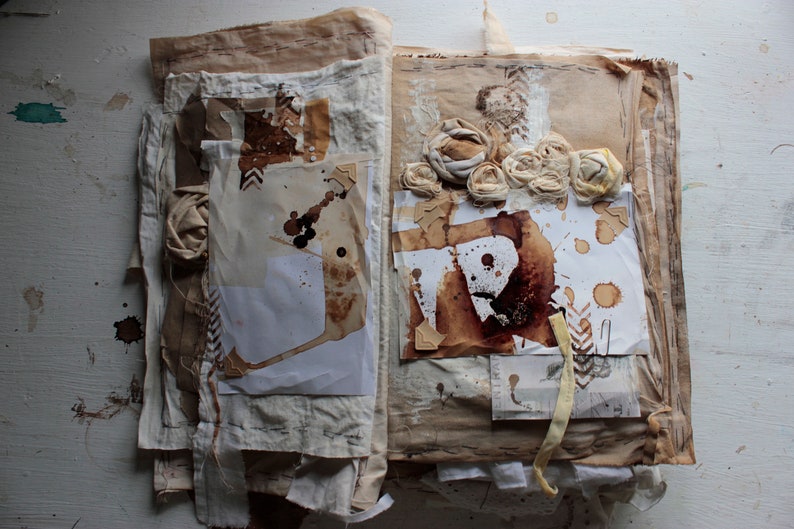 Puede incluir: Un libro abierto con p&aacute;ginas hechas de tela y papel superpuestos. Las p&aacute;ginas est&aacute;n decoradas con pintura marr&oacute;n y blanca, manchas de caf&eacute; y flores de tela.
