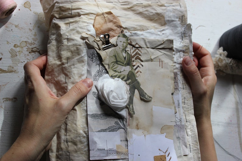 Puede incluir: Un collage vintage con una foto en blanco y negro de un hombre con traje sentado en una silla. El collage est&aacute; hecho en un trozo de papel marr&oacute;n con una flor de tela blanca y otros recortes de papel.