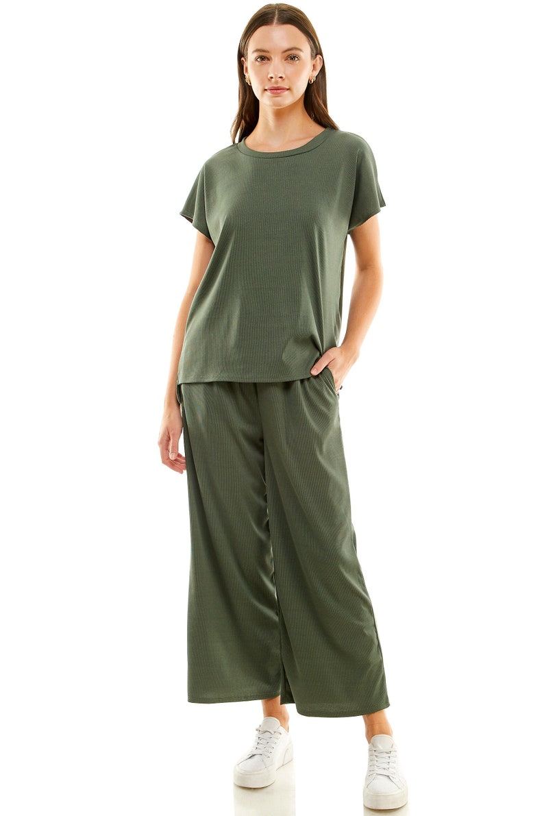May include: A green two-piece outfit with a short-sleeved top and wide-leg trousers. The model is wearing white trainers.
