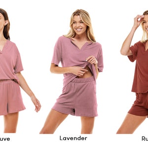 May include: Three women model matching short-sleeved tops and shorts sets in mauve, lavender, and rust colors. The sets are made of a soft, ribbed fabric.