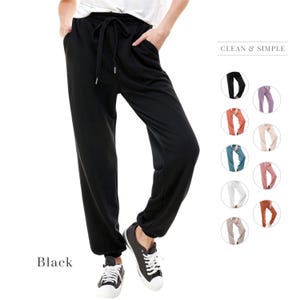 May include: Black sweatpants with a drawstring waist and cuffed legs. The sweatpants are shown on a model wearing black sneakers. The image also shows a variety of colors for the sweatpants, including teal, pink, red, and white.
