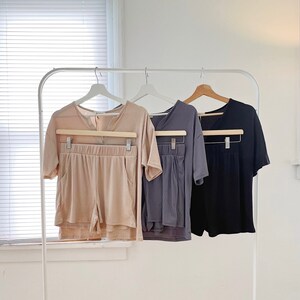 May include: Three sets of matching pajamas, one in beige, one in gray, and one in black, hanging on a white rack.