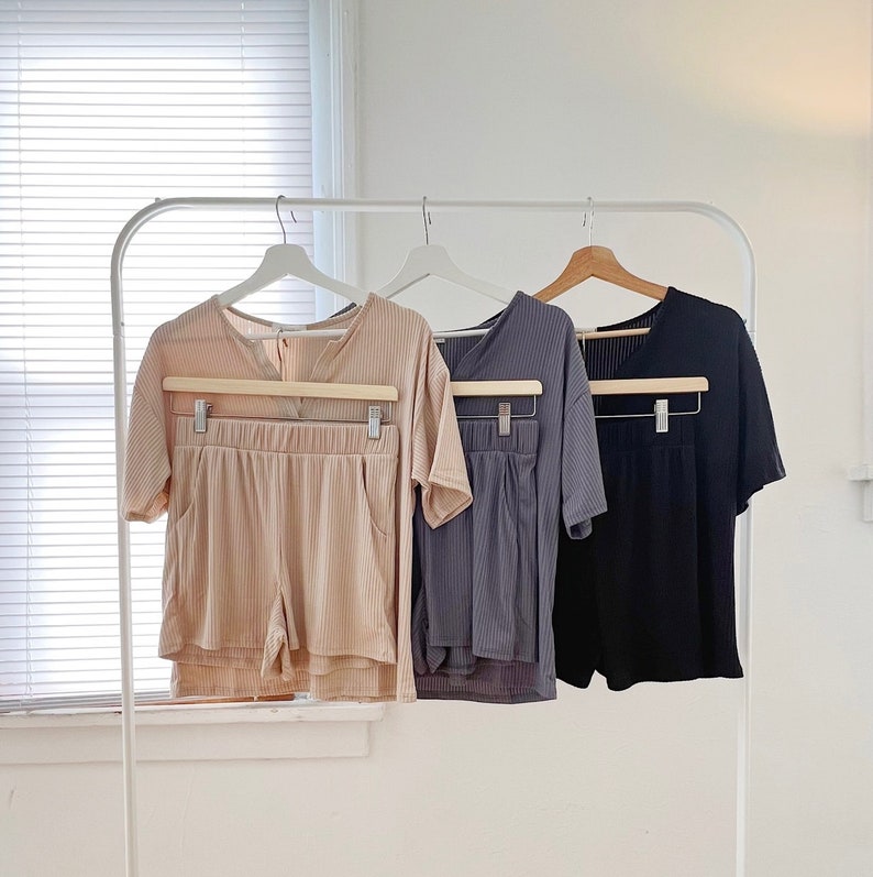 May include: Three sets of matching pajamas, one in beige, one in gray, and one in black, hanging on a white rack.