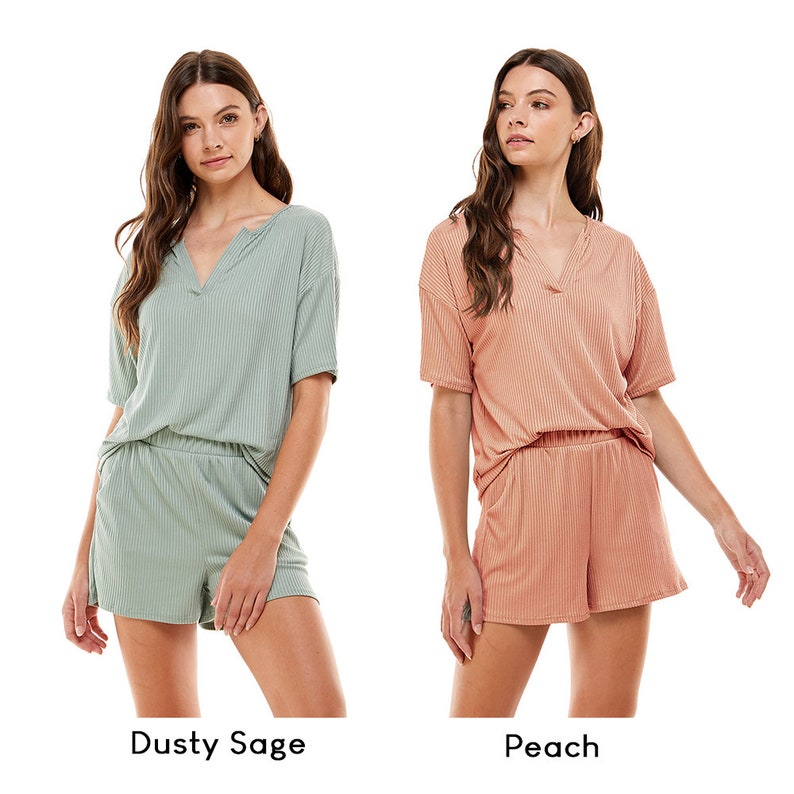 May include: Two women wearing matching ribbed short-sleeved tops and shorts. The woman on the left is wearing a dusty sage green set, and the woman on the right is wearing a peach set. Both tops have a V-neckline.