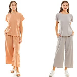 May include: Two women wearing matching short-sleeved tops and wide-leg trousers. The woman on the left is wearing a peach top and trousers, while the woman on the right is wearing a grey top and trousers.