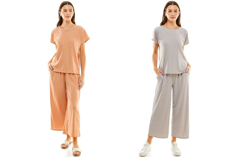 May include: Two women wearing matching short-sleeved tops and wide-leg trousers. The woman on the left is wearing a peach top and trousers, while the woman on the right is wearing a grey top and trousers.