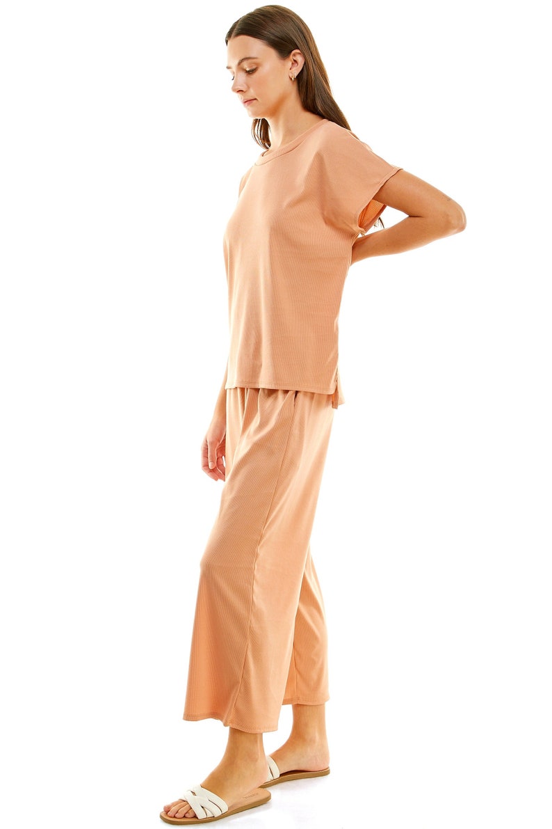 May include: A peach-coloured two-piece lounge set with a short-sleeved top and wide-leg trousers. The model is wearing the set and white sandals.