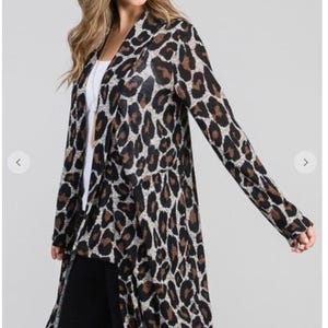 A blonde model wearing a long grey and brown animal print cardigan over a white shirt and black pants against a plain grey background.