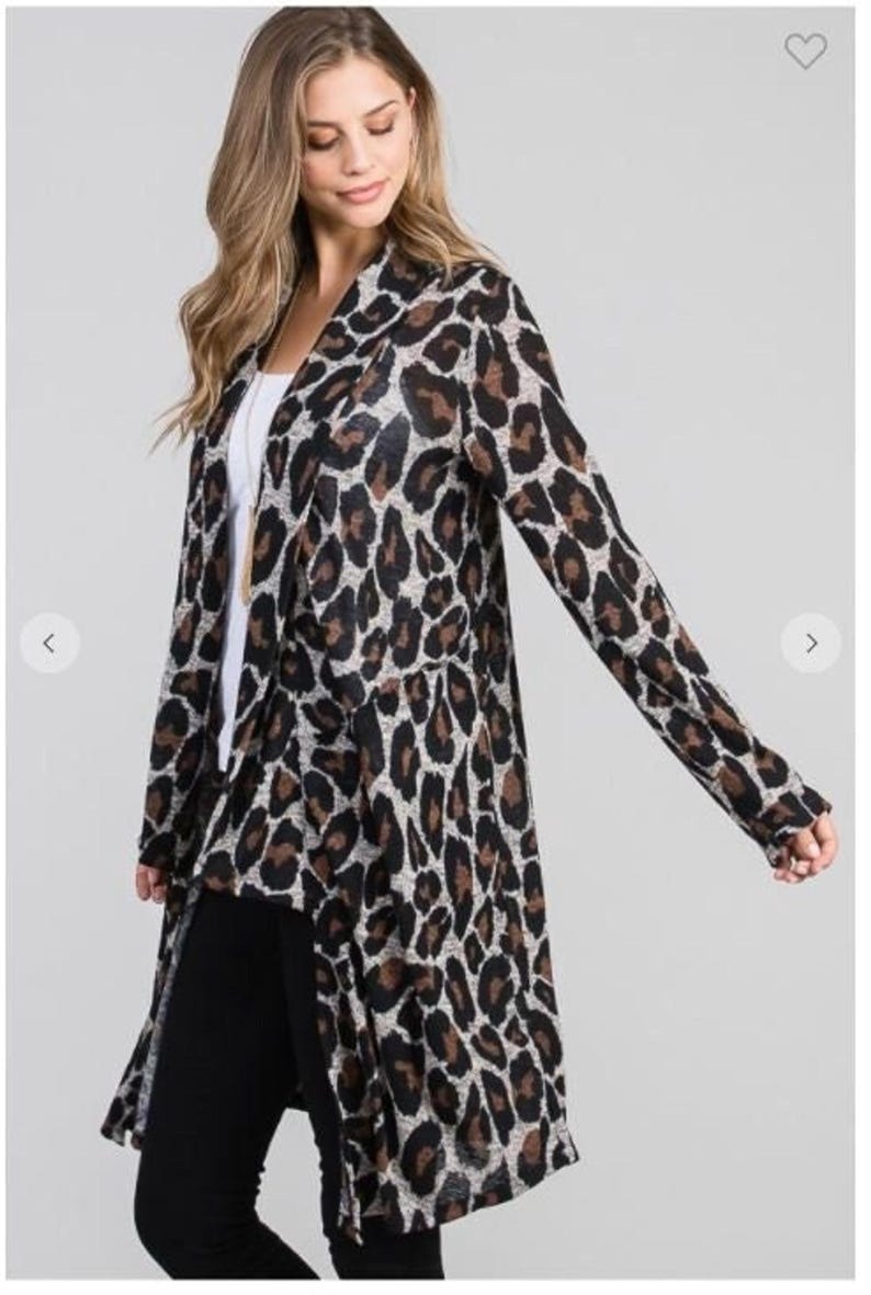 A blonde model wearing a long grey and brown animal print cardigan over a white shirt and black pants against a plain grey background.