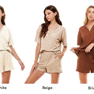 May include: Three women model matching short-sleeved tops and shorts sets in off-white, beige, and brick colors. The tops have a V-neck and a button detail. The shorts have an elastic waistband.