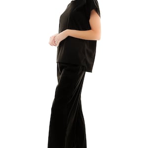 May include: A black velvet top and matching wide-leg trousers. The top has a round neckline and short sleeves. The trousers have a straight leg and a relaxed fit.