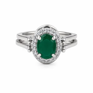 May include: A silver-toned ring featuring a central oval-cut dark green gemstone surrounded by a halo of small clear stones. The band is split into two parallel sections on each side, connecting to the central setting with four prongs.