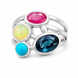 May include: A silver ring featuring four distinct gemstones: a faceted oval pink stone, a round iridescent opal, a round bright turquoise stone, and a large faceted oval dark blue stone, all set within a multi-band polished silver frame.