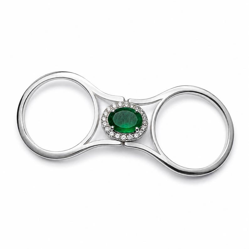 May include: A double-finger ring crafted from polished silver-toned metal, featuring a central oval-cut deep green gemstone surrounded by a halo of small, clear, round-cut stones. The design connects two circular bands with a central bridge.