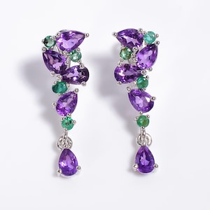 May include: A pair of drop earrings featuring multiple pear-cut purple amethyst stones and round-cut green emerald stones set in silver-toned metal. The design consists of a cluster of stones at the top with a single dangling pear-cut amethyst.