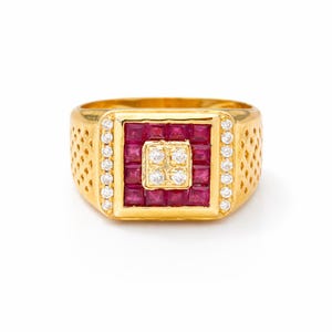 Könnte beinhalten: Ein goldener Ring mit quadratischer Fassung. Die Fassung ist mit einem Quadrat aus roten Edelsteinen besetzt, umgeben von einer Bordüre aus kleinen weißen Edelsteinen. Das Band des Rings hat ein strukturiertes Design.