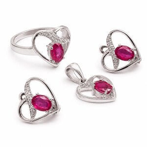 Op de afbeelding: Een sieradenset bestaande uit een ring, een hanger en twee oorbellen. Elk stuk heeft een zilverkleurig hartvormig frame met een centrale ovaal geslepen dieproze edelsteen en kleine heldere steentjes langs de rand van het hart.