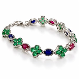 Puede incluir: Una pulsera de tono plateado con eslabones alternos en forma de trébol de cuatro hojas engastados con piedras verdes y eslabones ovalados con piedras azules y rojas. La pulsera incluye un cierre de mosquetón y una cadena de extensión.