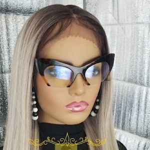 Könnte beinhalten: Eine lange, glatte, blonde Perücke mit dunklen Ansätzen. Die Perücke ist mit einem Mittelscheitel gestylt und hat einen natürlichen, fließenden Look. Die Perücke wird von einer Puppe mit schwarzem Eyeliner und rosafarbenem Lippenstift getragen. Die Puppe trägt schwarze und weiße Ohrringe. Das Bild enthält den Text "Enjoy Life Wigs".