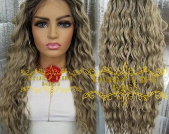 May include: A long, wavy, light brown and blonde wig with a lace front. The wig is styled in loose waves and has a natural-looking hairline.