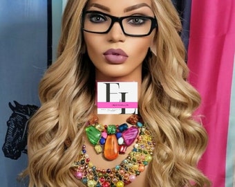 May include: A mannequin head with long, wavy blonde hair, wearing black-framed glasses and a colorful statement necklace. The mannequin has a logo covering the face. The background features a mix of colors and patterns.