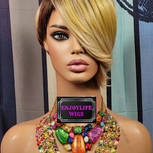 May include: A blonde and brown wig with a side parting and bangs. The wig is styled in a short bob with layers. The wig is on a mannequin head with a colourful beaded necklace. The text "ENJOYLIFE WIGS" is on a black sign.