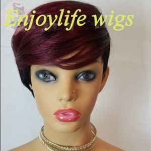 Può includere: Una parrucca corta, liscia, di colore bordeaux e nero con frangia. La parrucca è acconciata su una testa di manichino. Il testo "Enjoylife wigs" è visibile nella parte superiore centrale dell'immagine.