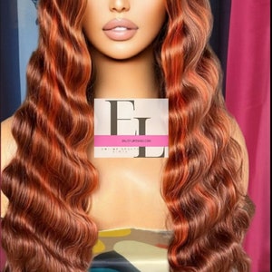 May include: A long, wavy, auburn-colored wig with highlights. The wig is styled in loose waves and has a natural-looking parting. The wig is worn by a model with a neutral expression. The text "ENJOYWIGS.COM" is visible on a white card in the image.