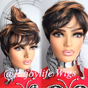 May include: A short, choppy, black and brown wig with a side part and bangs. The wig is styled with a messy, textured look. The wig is worn by a mannequin with a red shirt and silver jewelry.
