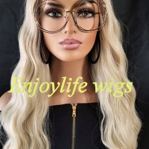May include: A blonde wavy wig on a mannequin head. The wig is styled in loose waves and has a natural-looking finish. The mannequin is wearing a black top with a gold zipper. The text "Enjoylife wigs" is visible in the image.