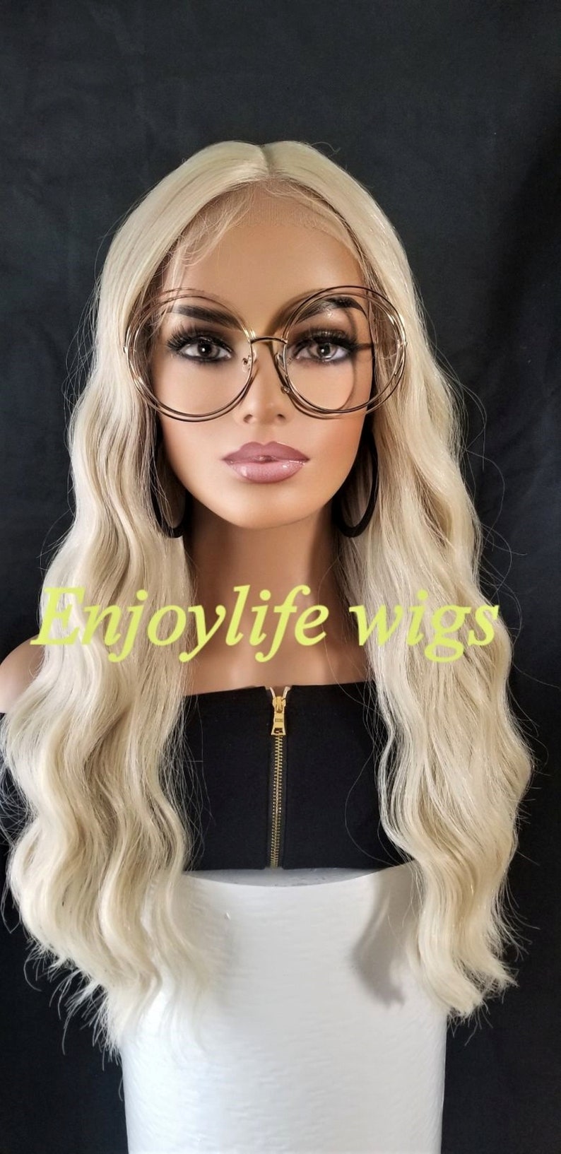 May include: A blonde wavy wig on a mannequin head. The wig is styled in loose waves and has a natural-looking finish. The mannequin is wearing a black top with a gold zipper. The text "Enjoylife wigs" is visible in the image.