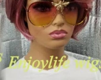 May include: A short, pink and black wig with side-swept bangs. The wig is styled in a modern, edgy bob.