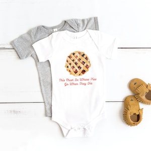 May include: White baby onesie with a red and brown pie graphic and the text "This Must Be Where Pies Go When They Die".